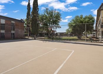 A large, empty parking lot with a building and trees in the background.